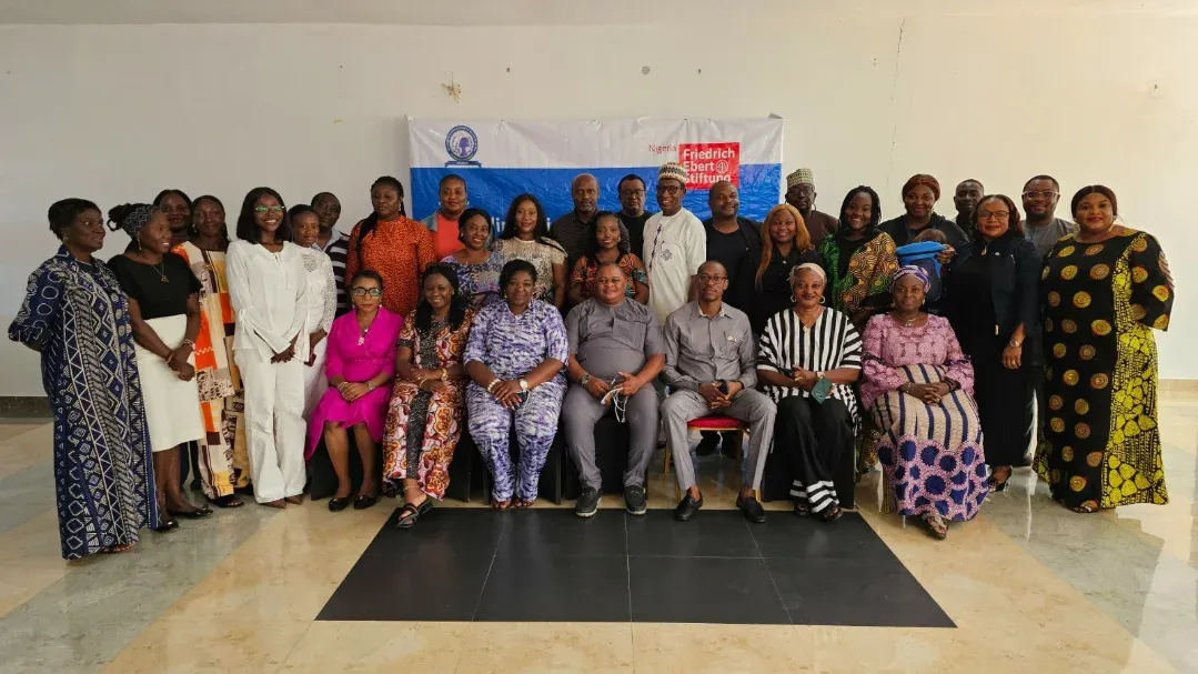 A large mixed group posing with an institutional banner in a conference hall