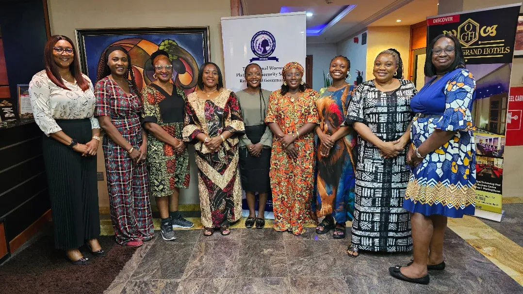 Women in patterned dresses standing with a banner at a hotel function