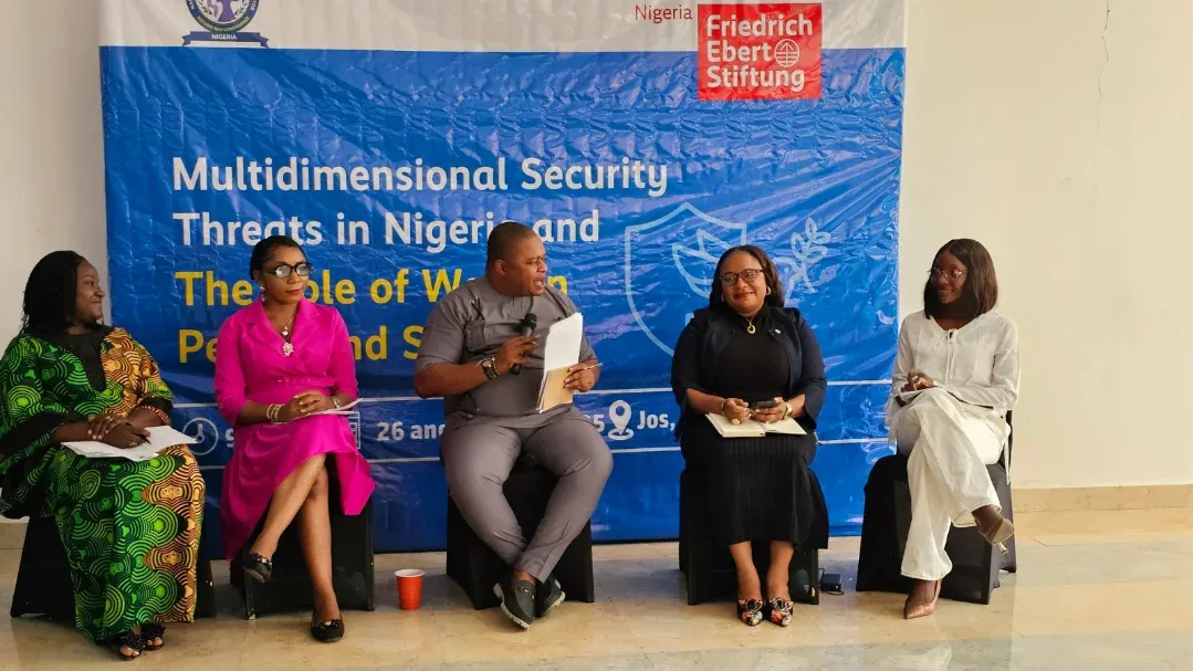 Five women seated on a stage in front of a blue event backdrop during a panel