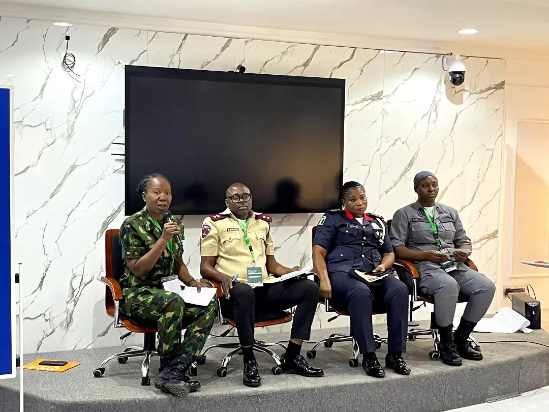 Women in military and police uniform seated on a stage during a panel discussion